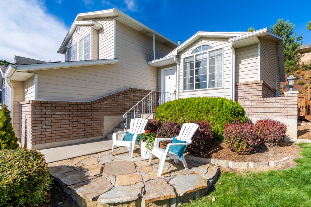 Residential exterior with a front entrance, patio chairs, and planted borders